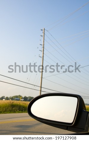 A side mirror of a car driving past some power lines.