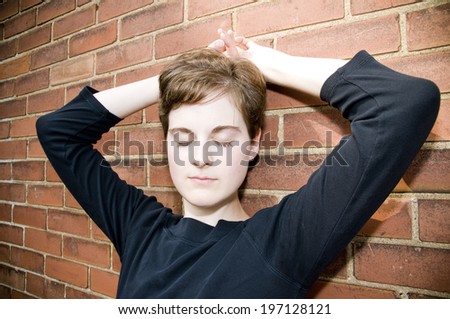 A young person stands against a brick wall.
