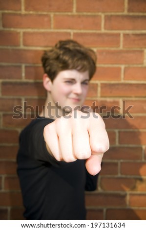 A woman against a brick wall with a fist out in selective focus.
