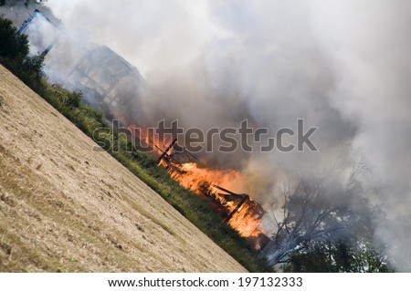 A building burning with smoke, trees and grass.