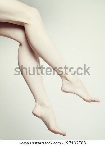Slim legs of a white woman wearing no shoes or socks.