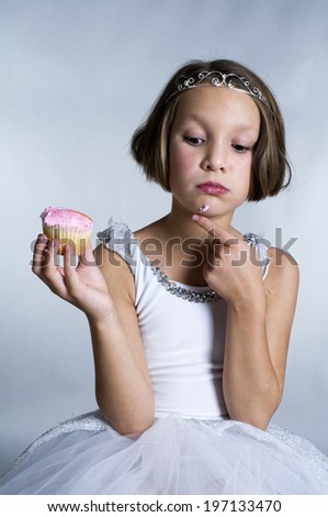 A young girl wearing a tiara and a dressing up costume, holding a cupcake.