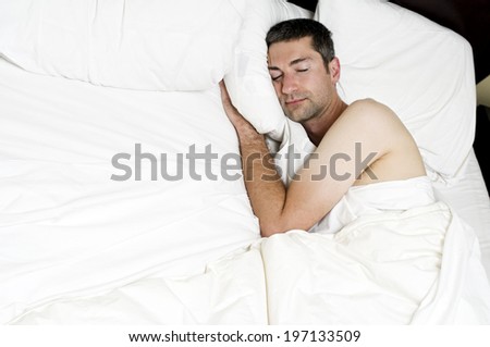 A man sleeping in a bed with white sheets and pillow cases.