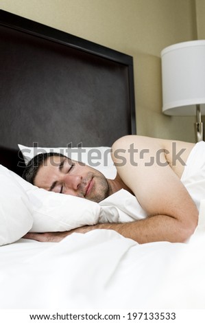 A man sleeping in bed with his hand under the pillow.