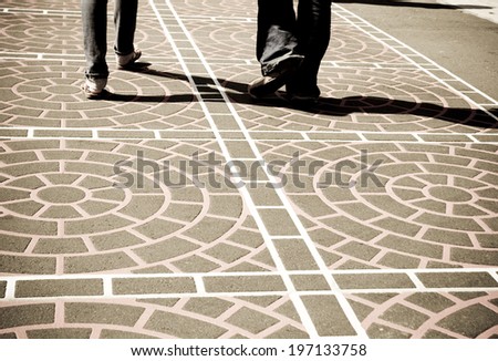 Two people walking across a tiled walk way.
