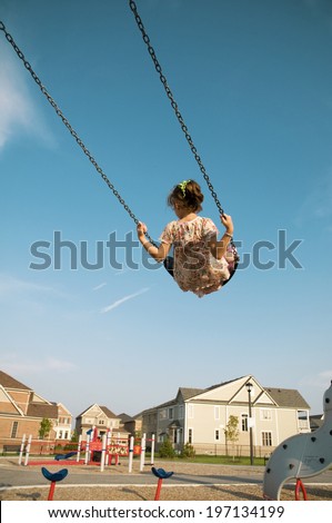 A little girl swinging high on a swing at the playground.