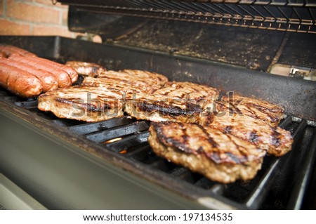Hamburgers and hot dogs cooking on an outdoor grill.