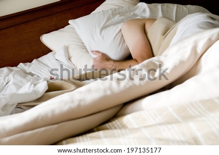 A person lies in bed with a pillow over their head.