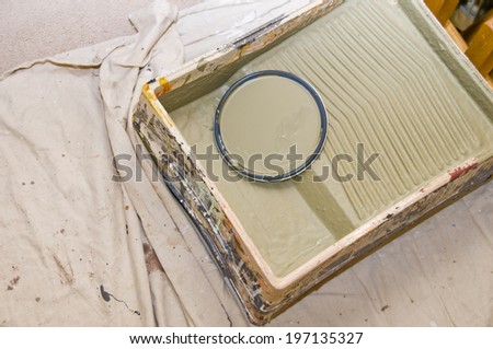 A paint can lid in a roller tray on a white drop cloth.