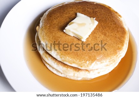 A stack of pancakes with syrup and a pat of butter on a white plate.