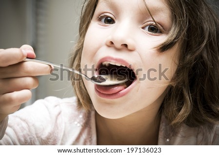 A young girl eating cereal from a spoon.