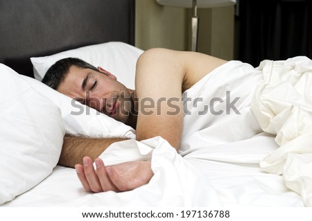 A man asleep in a bed with pillows and sheets.