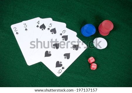 Poker chips, playing cards and dice are arranged on a green surface.