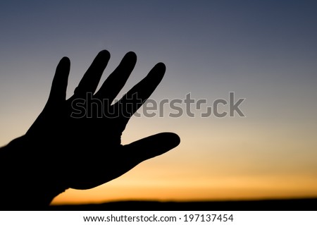 A person\'s hand silhouetted against a setting sun.