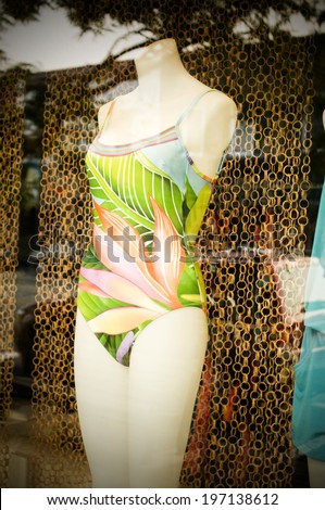 A mannequin in a store window is wearing a bathing suit.