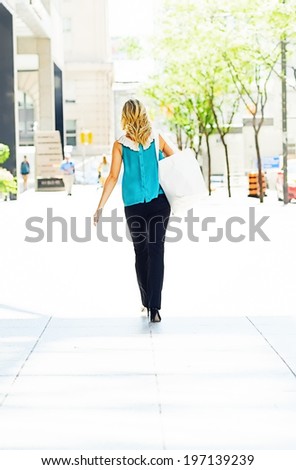 A woman with bags walking away down a street.
