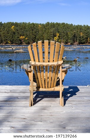 A wooden lawn chair on a deck overlooking a lake.