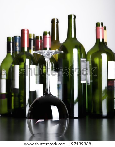 A half-full, upside down wine glass in front of several empty wine bottles.