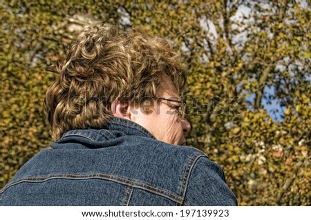 A person wearing a denim jacket while standing near trees.