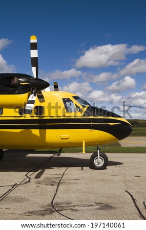 The front of a yellow and black airplane, and a clear sky with a few clouds.