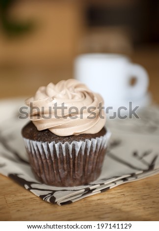 A chocolate cupcake with frosting on a linen napkin placed on a wooden table.