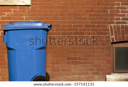 A blue garbage bin against a brick wall.