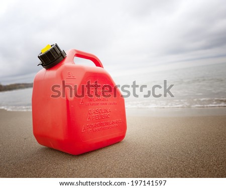 A red fuel container sitting on the sand at the beach.