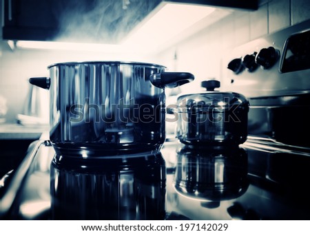 A large metal pot emitting steam on a stove top with another smaller pot.