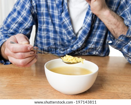 A man wearing a plaid shirt and white under shirt eating soup.