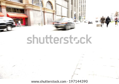 Cars drive along a busy high street while pedestrians shop.