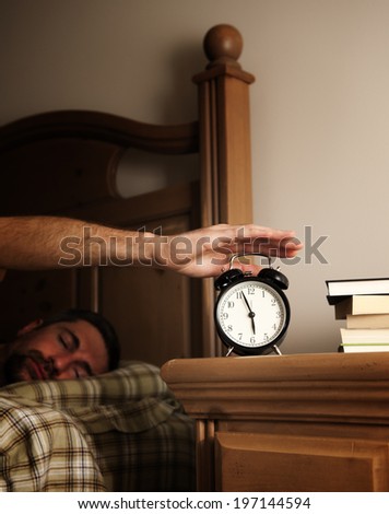A sleeping man is reaching for the alarm clock.