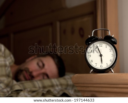 A sleeping man lies next to a manual alarm clock.
