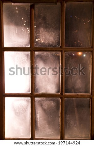 Fogged window with nine small rectangular panes in wooden frame.