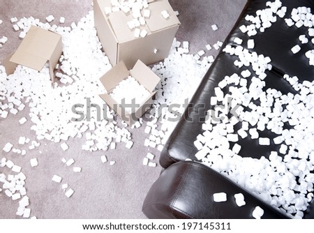 Styrofoam packing peanuts covering cardboard boxes and a sofa.