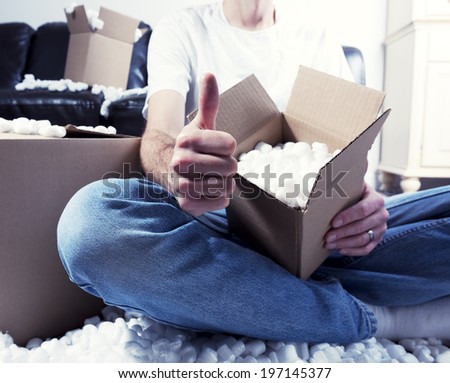A man surrounded by packing peanuts is giving a thumbs up.