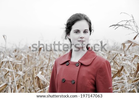 A lady in a red coat standing in a corn field.