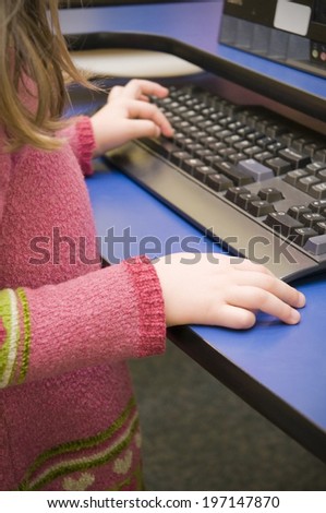 A little girl in a pink jumper using a desktop computer.