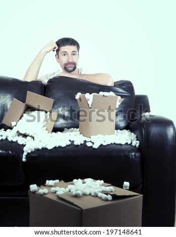 A man who is behind a black leather couch that has cardboard boxes on it.