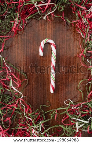 A striped candy cane on a wood surface surrounded by colored paper shreds.