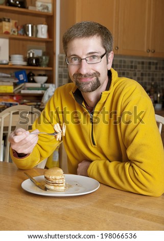 A man in a yellow sweater seated at a table with half eaten pancakes.