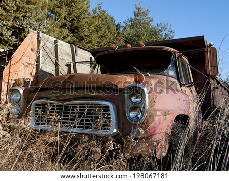 An old truck rusting outside on a sunny day.