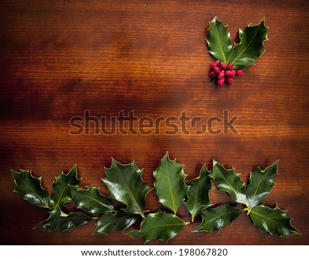Green holly leaves in a pattern on a wooden desk.