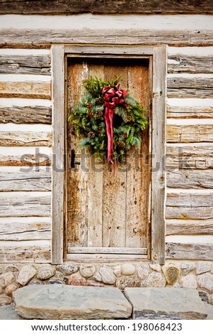 A wreath with a red bow on a wooden door in a wood cabin.