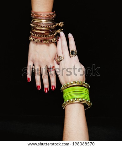 Two human arms covered with many colorful bracelets.