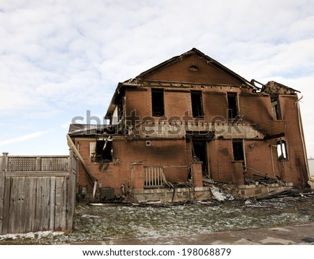 An old, burned out house sits deserted with a fence.