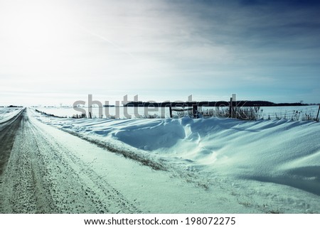 A road covered with snow stretches across a snow-covered flat landscape.