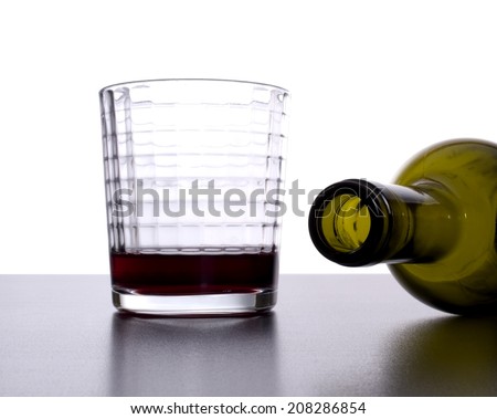 Empty wine bottle tipped over next to nearly empty glass