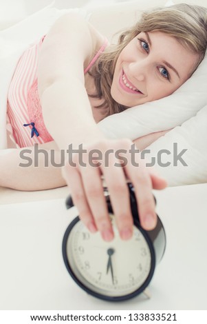 A young woman reaching for the snooze button on his alarm clock with selective focus.
