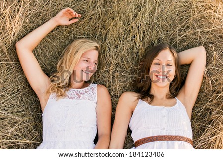 two girlfriends lying down on grass laughing having good time. Summer vacation.