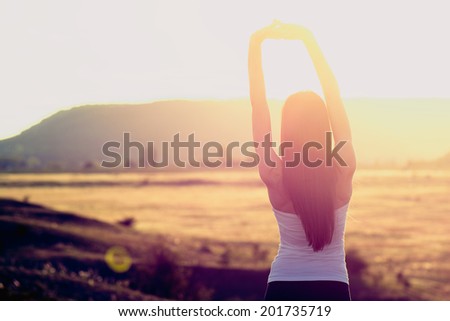 Happy celebrating winning success woman at sunset or sunrise standing elated with arms raised up above her head